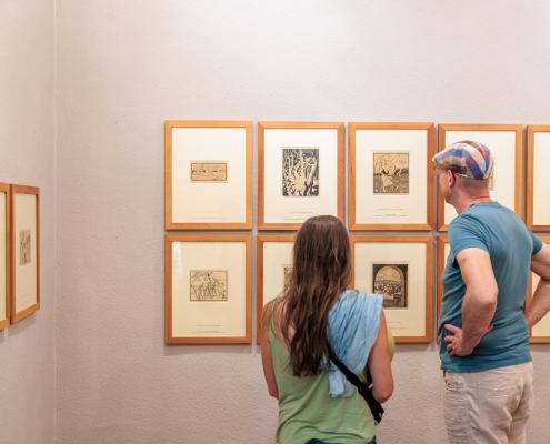 Besucher in einem Museum, die eine Sammlung von Grafiken betrachten.