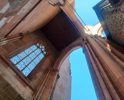 Blick nach oben im Wetzlarer Dom Blick von unten in den nach oben hin offenen, unvollendeten Westbau des Wetzlarer Doms. Links ist ein großes gotisches Maßwerkfenster mit blauem Glas zu sehen, während mächtige, rötliche Sandsteinpfeiler und Spitzbögen den Blick auf den blauen Himmel freigeben.