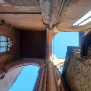 Die Perspektive zeigt den Blick steil nach oben in die unvollendete, zum Himmel offene Westfassade des Wetzlarer Doms. Die massiven Pfeiler und Spitzbögen aus rötlichem Sandstein rahmen den blauen Himmel ein, während links ein gotisches Maßwerkfenster mit blauem Muster erkennbar ist und rechts eine kontrastierende, dunklere Steinwand aufragt.