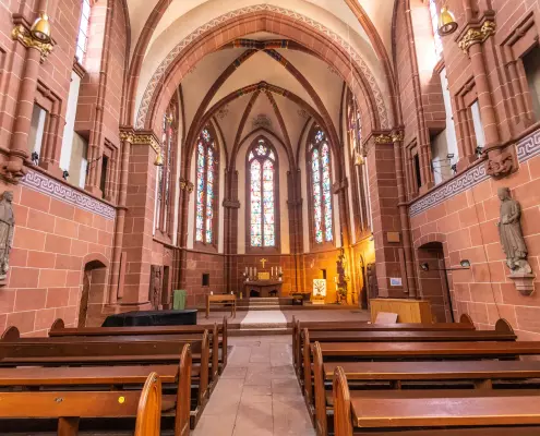 Mittelgang im gotischen Chorraum des Wetzlarer Doms Blick durch den von Holzkirchenbänken gesäumten Mittelgang in den gotischen Chorraum des Wetzlarer Doms, dessen hohe Spitzbogenfenster mit bunten Glasmalereien verziert sind. Die Wände bestehen aus rötlichem Sandstein, sind mit Steinstatuen geschmückt und münden nach oben hin in ein ausgeprägtes Kreuzrippengewölbe.