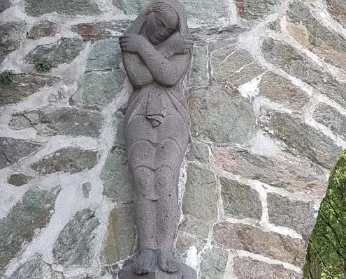 Steinskulptur einer trauernden oder schlafenden Frau Das Bild zeigt eine Steinskulptur einer trauernden oder schlafenden Frau, die im Stil eines Reliefs oder einer Wandkonsole an einer Natursteinmauer angebracht ist.