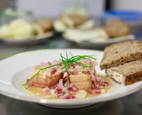 Handkäse mit Musik „Ein Teller mit mariniertem Handkäse mit Musik, garniert mit feinen roten Zwiebelwürfeln und Schnittlauch, serviert mit zwei Scheiben frischem Graubrot.“